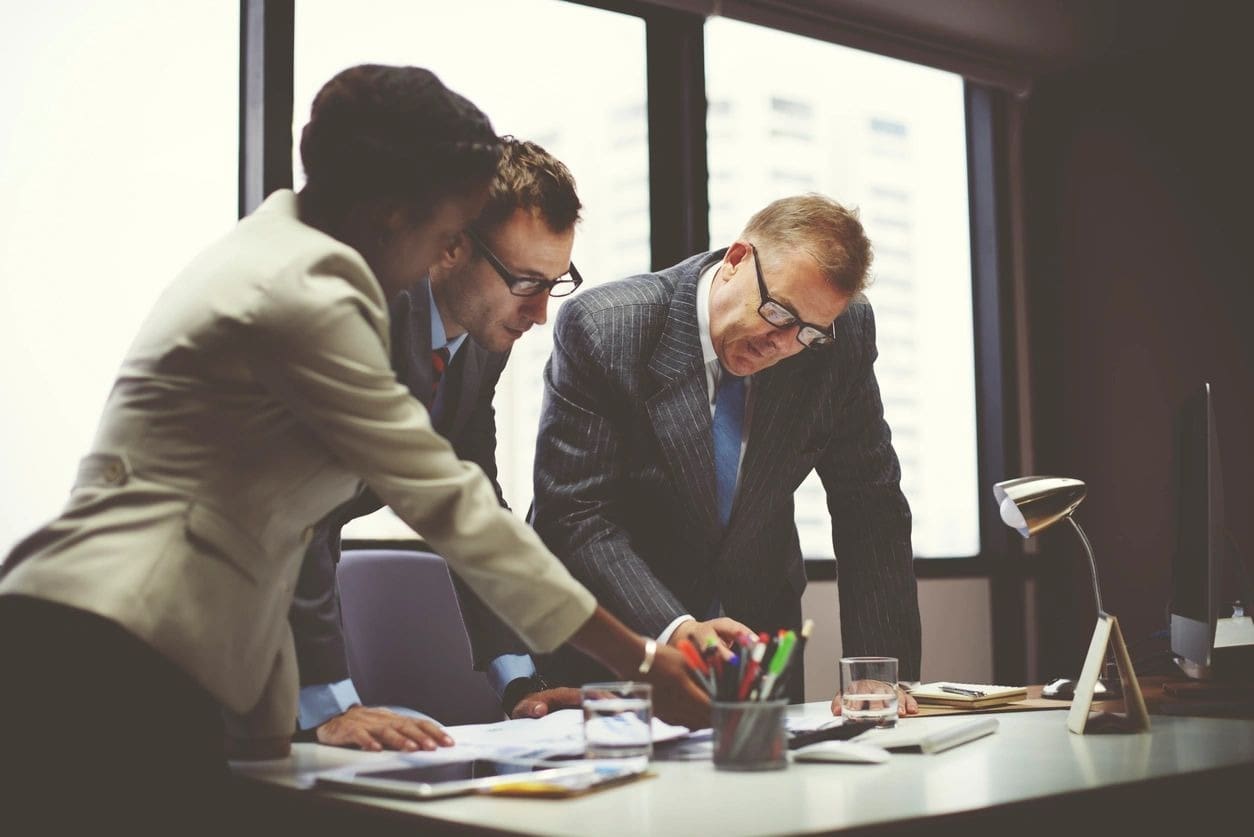 Three men in suits and ties working on papers.